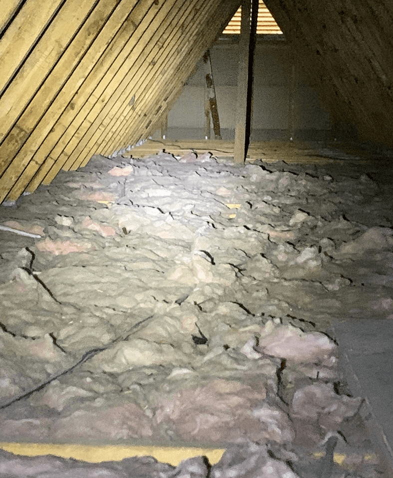 Attic with exposed insulation and wooden beams.