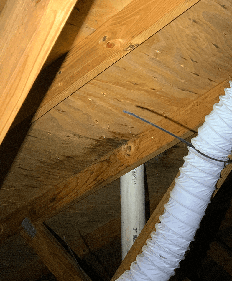 Wooden attic beams with ductwork and pipe.