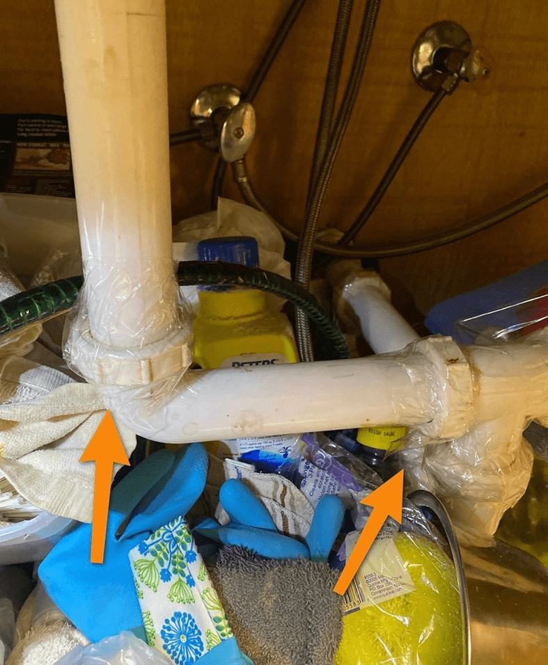 Leaking pipes under sink with arrows.
